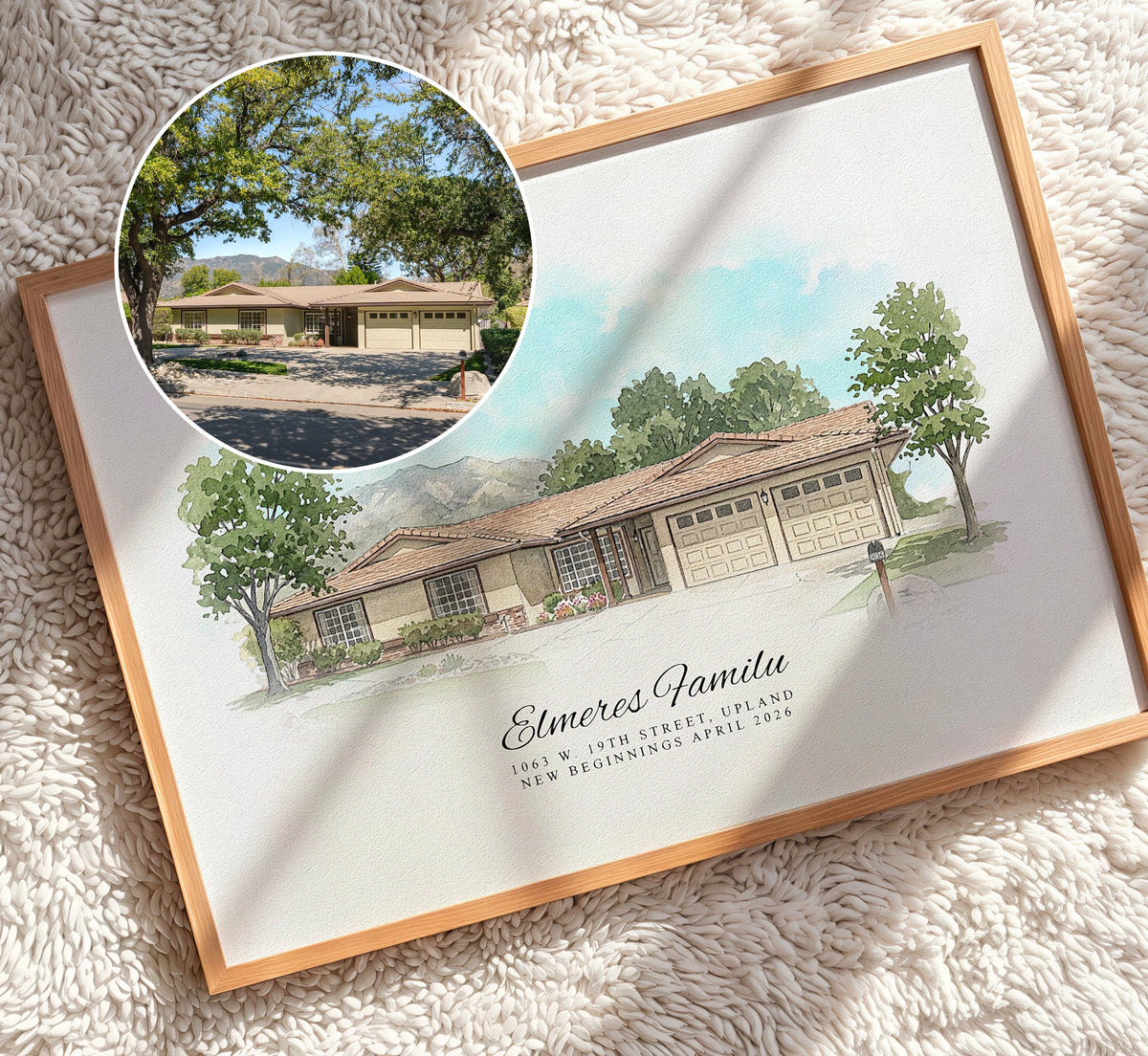 A framed custom watercolor house illustration print featuring a single-story home with garage doors and the text 'Elmer's Family 1963 W 42nd Street Ranch New Registration April 2026.' A circular inset photo of the actual house appears in the top left, and the print is photographed on a cream shag rug with soft shadows across it.