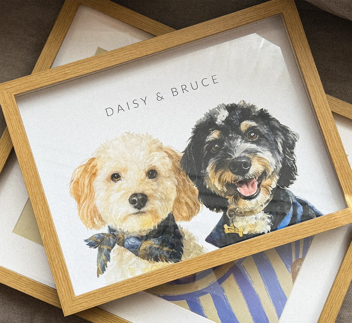 Framed watercolor artwork of two dogs with 'Daisy & Bruce' text on a striped surface.