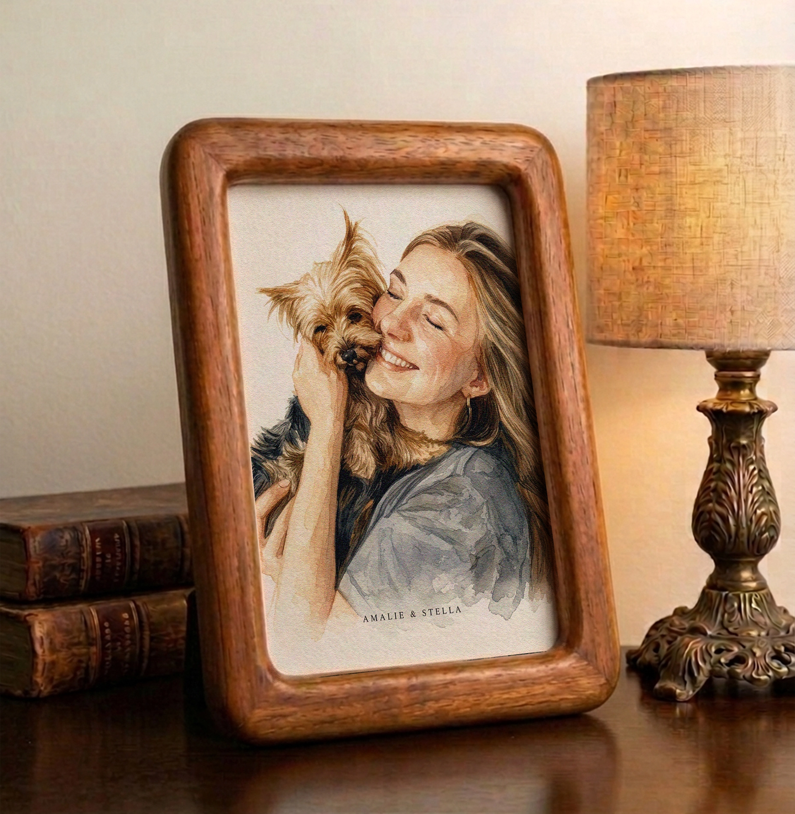 A soft watercolor illustration of a smiling woman hugging her small dog, titled "Amalie & Stella," shown in a modern wood frame mockup.