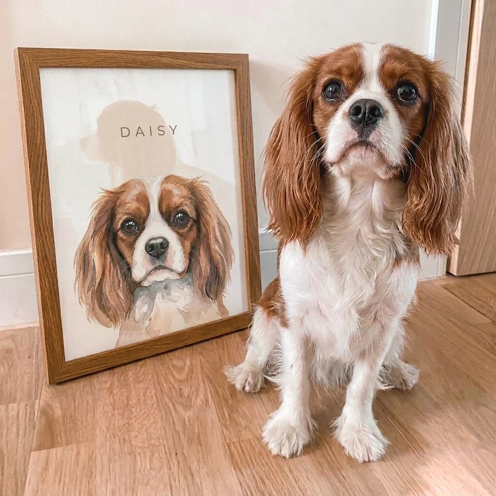 Dog sitting next to a framed portrait of itself named 'Daisy' on a wooden floor.